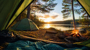 widok z namiotu na jezioro o zachodzie słońca z ogniskiem i rozbitym namiotem