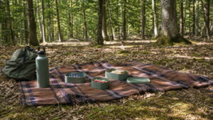 Piknik w lesie z kocem, pojemnikami wielorazowymi i bidonem bez śmieci w otoczeniu drzew.